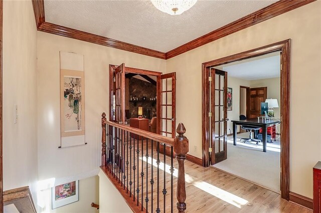 corridor featuring french doors, ornamental molding, a textured ceiling, and light wood-type flooring