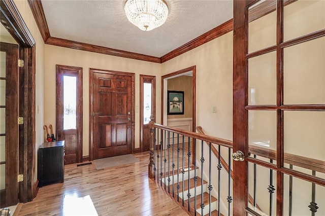 entryway featuring a chandelier, light hardwood / wood-style floors, a textured ceiling, and ornamental molding