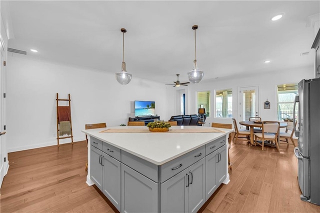 kitchen with pendant lighting, stainless steel refrigerator, gray cabinetry, a center island, and light hardwood / wood-style floors