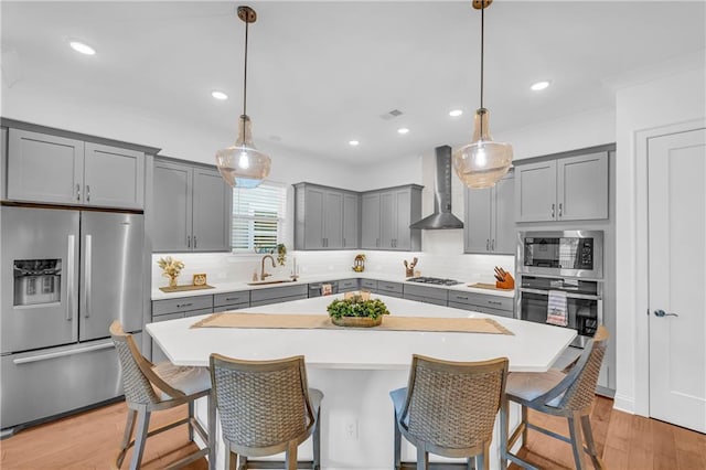 kitchen with pendant lighting, sink, stainless steel appliances, and wall chimney exhaust hood