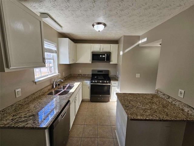 kitchen featuring stainless steel appliances, sink, white cabinetry, a textured ceiling, and dark stone counters