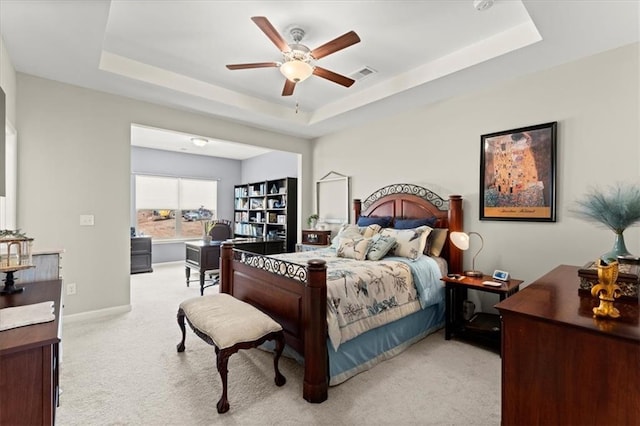 bedroom featuring ceiling fan, light colored carpet, and a tray ceiling