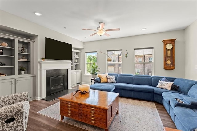 living room with dark hardwood / wood-style flooring, ceiling fan, and built in shelves