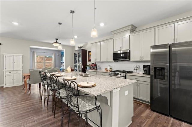 kitchen featuring stainless steel appliances, sink, light stone counters, pendant lighting, and a kitchen island with sink