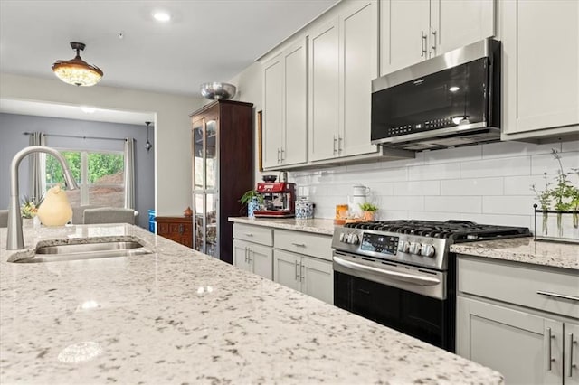 kitchen featuring appliances with stainless steel finishes, decorative backsplash, light stone countertops, and sink