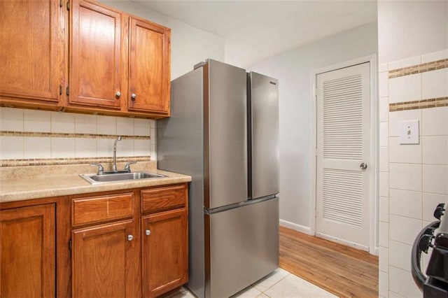 kitchen with light tile patterned floors, tasteful backsplash, stainless steel refrigerator, and sink