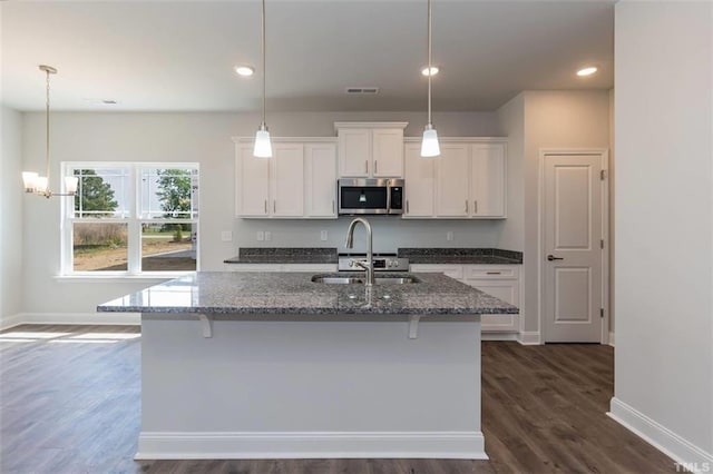 kitchen with a center island with sink, stainless steel microwave, dark stone countertops, white cabinetry, and a sink