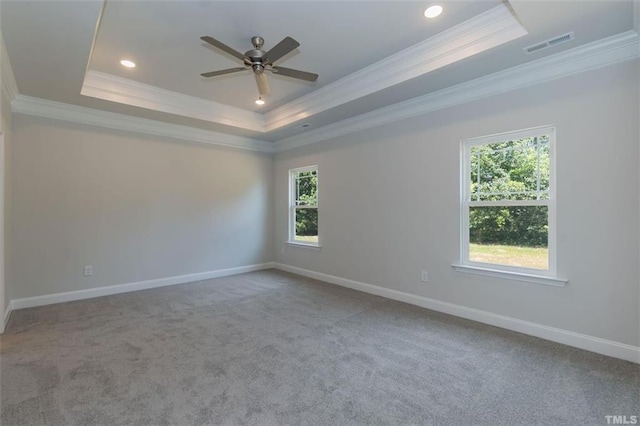 empty room with visible vents, a tray ceiling, baseboards, and ornamental molding