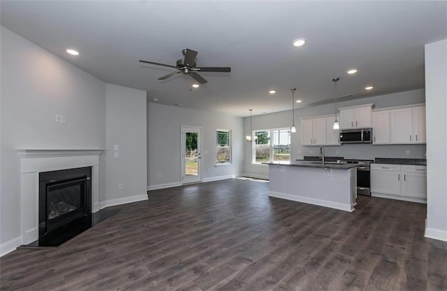 kitchen featuring a kitchen island with sink, stainless steel appliances, white cabinets, open floor plan, and dark countertops