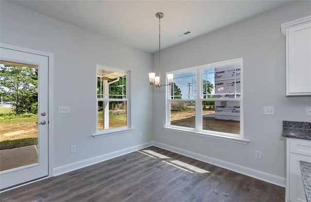 unfurnished dining area with dark wood-type flooring, visible vents, baseboards, and an inviting chandelier