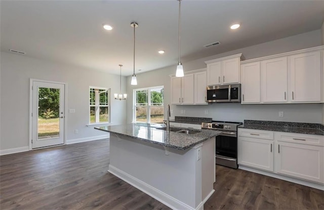 kitchen with stainless steel appliances, a sink, white cabinetry, hanging light fixtures, and a center island with sink