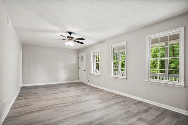 unfurnished room featuring healthy amount of natural light, wood finished floors, baseboards, a ceiling fan, and a textured ceiling