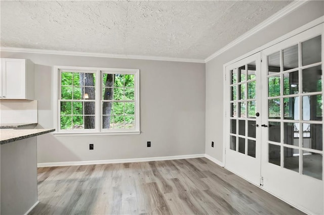 unfurnished dining area featuring a textured ceiling, crown molding, french doors, light wood-type flooring, and baseboards