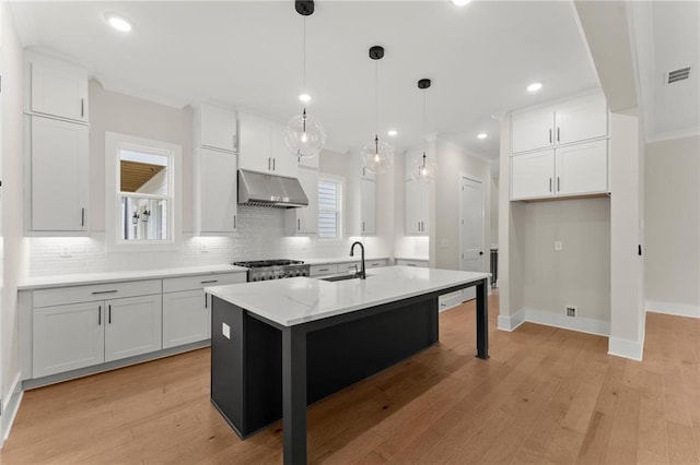 1419 Coretta Bnd, Atlanta, GA 30318 - kitchen featuring under cabinet range hood, backsplash, white cabinets, a center island with sink, and baseboards