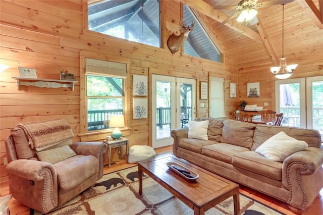 living room featuring ceiling fan with notable chandelier, wood walls, wood finished floors, wood ceiling, and beam ceiling