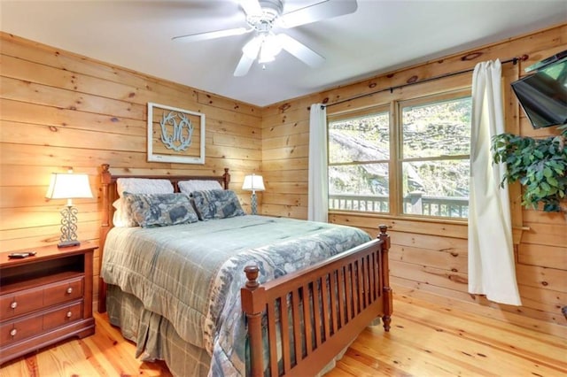 bedroom featuring light wood-style floors, wooden walls, and a ceiling fan