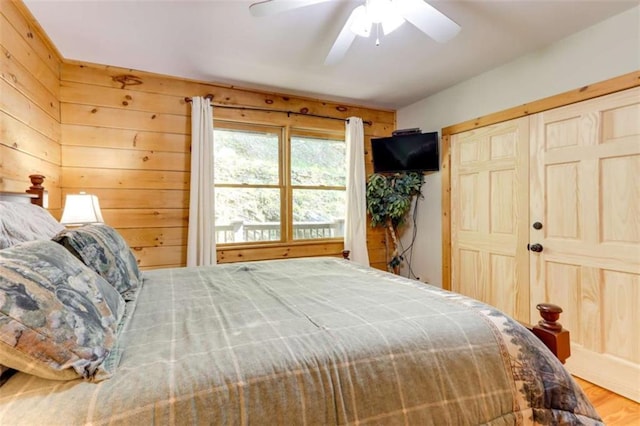 bedroom featuring a closet, wood walls, wood finished floors, and a ceiling fan