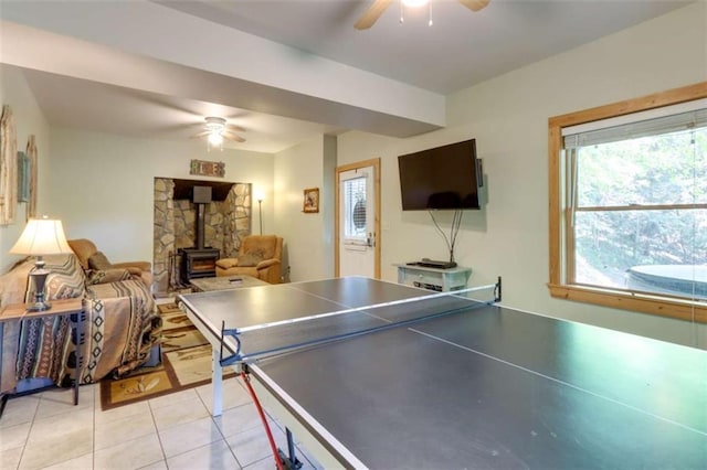 rec room with a wood stove, light tile patterned floors, and ceiling fan