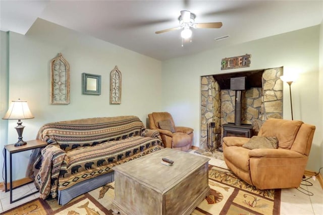 living room with visible vents, tile patterned floors, a wood stove, and a ceiling fan