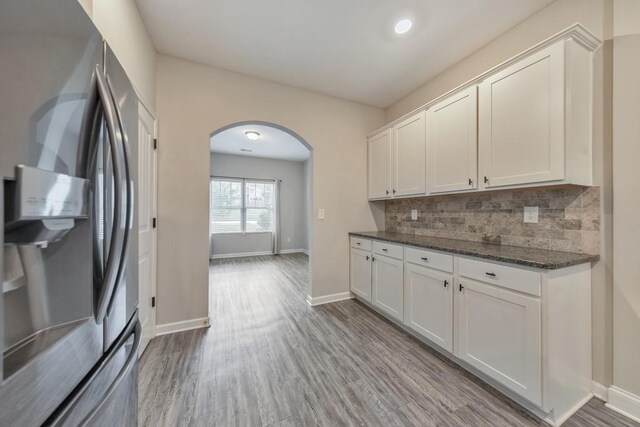 kitchen featuring stainless steel fridge, arched walkways, tasteful backsplash, and white cabinets