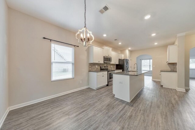 kitchen featuring appliances with stainless steel finishes, arched walkways, a chandelier, backsplash, and dark countertops