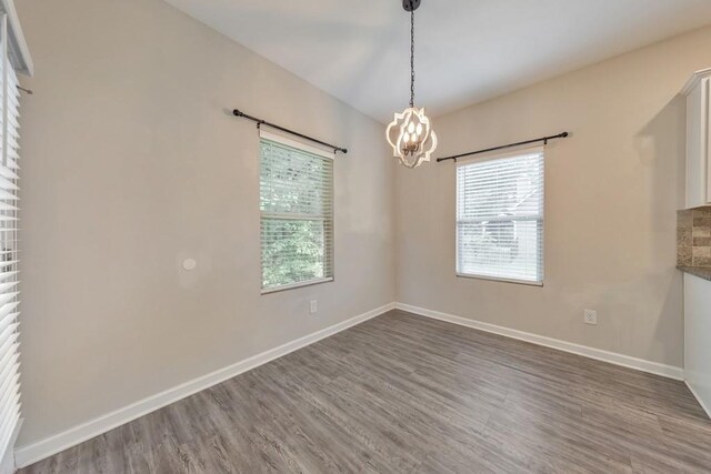 unfurnished room featuring a chandelier, wood finished floors, and baseboards
