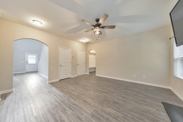 unfurnished room with arched walkways, ceiling fan, wood finished floors, and baseboards