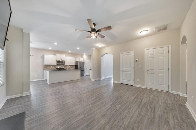 unfurnished living room featuring a ceiling fan, arched walkways, baseboards, dark wood finished floors, and recessed lighting