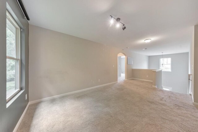 spare room featuring arched walkways, carpet floors, baseboards, and track lighting