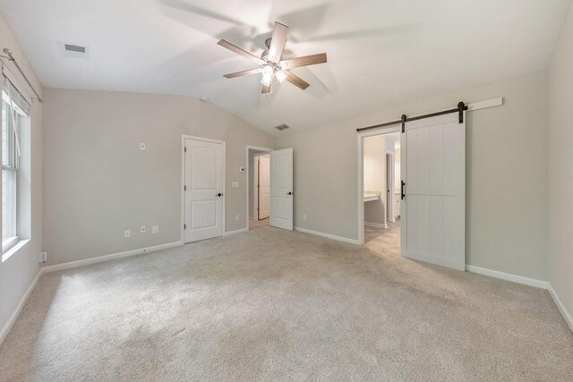 unfurnished bedroom with a barn door, vaulted ceiling, light carpet, multiple windows, and baseboards