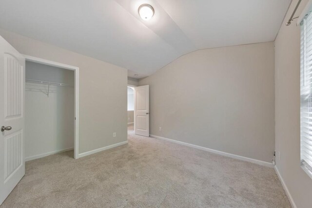 unfurnished bedroom with lofted ceiling, carpet, a closet, and baseboards