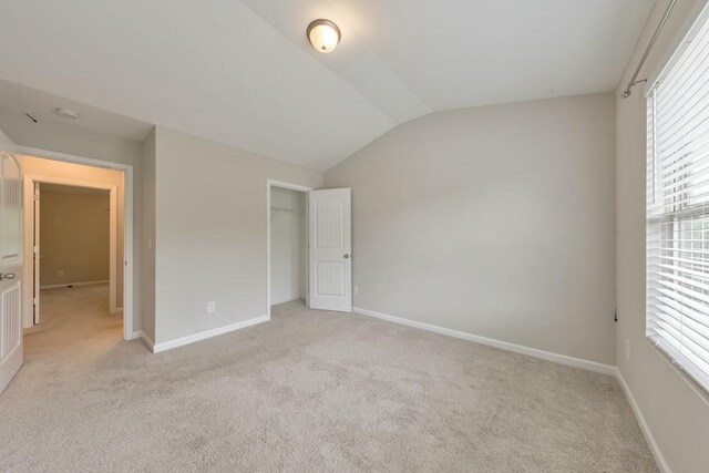 unfurnished bedroom featuring lofted ceiling, light colored carpet, baseboards, multiple windows, and a closet