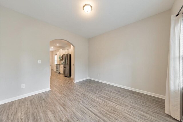 unfurnished room with arched walkways, wood finished floors, and baseboards