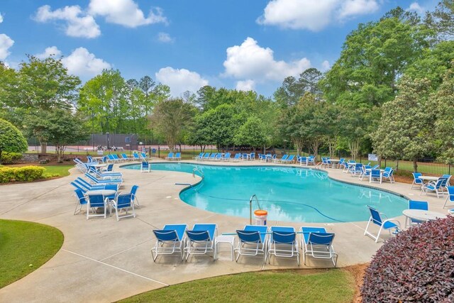 community pool with fence, a patio area, and view of wooded area
