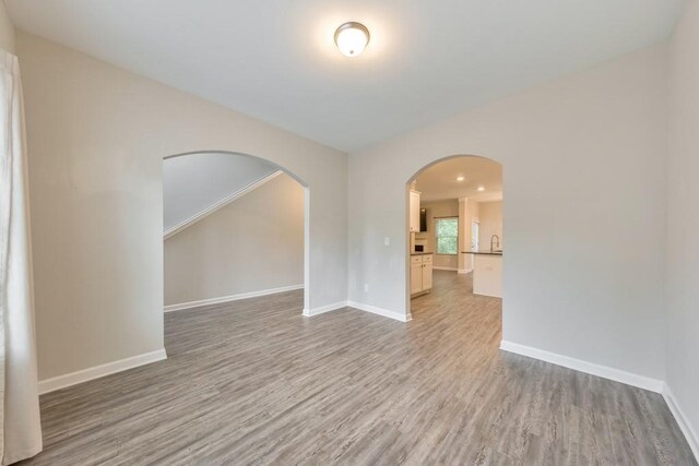 spare room featuring wood finished floors, baseboards, and arched walkways
