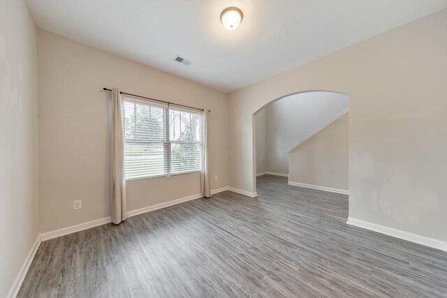 unfurnished room with arched walkways, wood finished floors, and baseboards