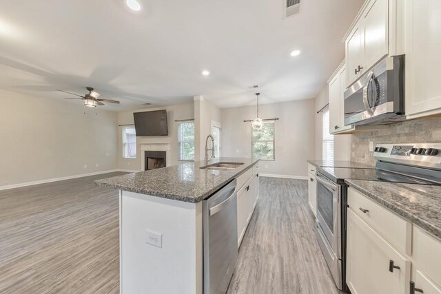 kitchen featuring appliances with stainless steel finishes, a sink, a ceiling fan, light wood-style flooring, and baseboards