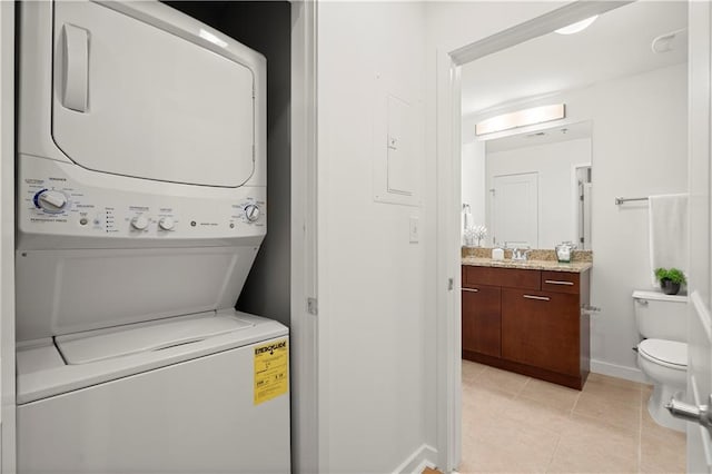 laundry area featuring light tile patterned flooring, sink, and stacked washer / drying machine