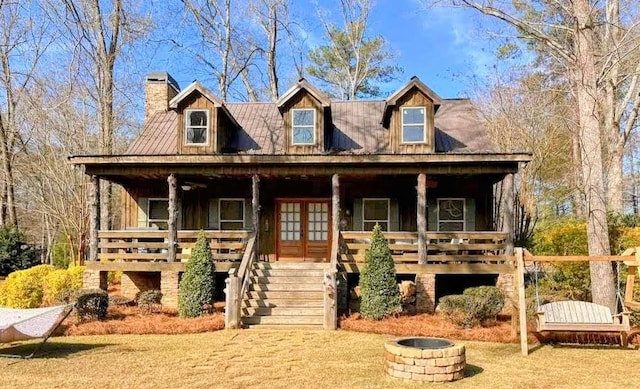 view of front of house featuring french doors, a chimney, covered porch, metal roof, and a fire pit