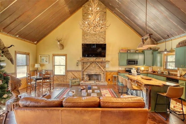 living room featuring a wainscoted wall, a fireplace, a notable chandelier, wooden walls, and high vaulted ceiling