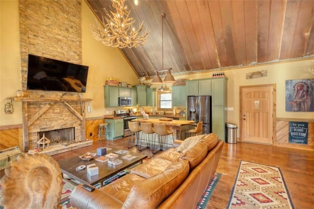 living room with an inviting chandelier, wood ceiling, a stone fireplace, high vaulted ceiling, and light wood-type flooring