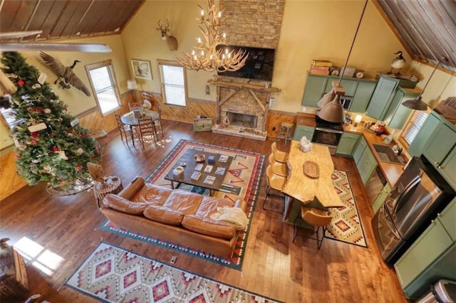 living room with a wainscoted wall, a notable chandelier, a fireplace, vaulted ceiling, and hardwood / wood-style flooring