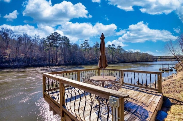 view of dock with a water view, outdoor dining area, and a wooded view