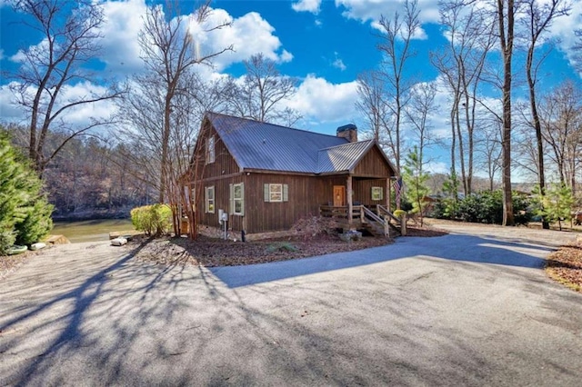 view of home's exterior featuring driveway, a chimney, and metal roof