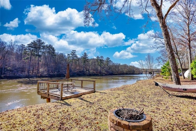 dock area featuring a water view, an outdoor fire pit, and a wooded view