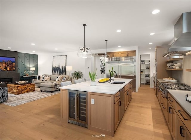 kitchen featuring wine cooler, sink, island range hood, hanging light fixtures, and a center island with sink