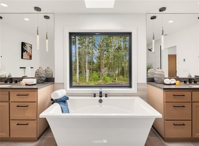 bathroom featuring tile patterned flooring, vanity, a washtub, and a skylight