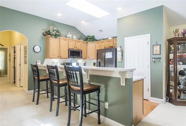 kitchen with light brown cabinets, lofted ceiling, appliances with stainless steel finishes, tasteful backsplash, and a breakfast bar area