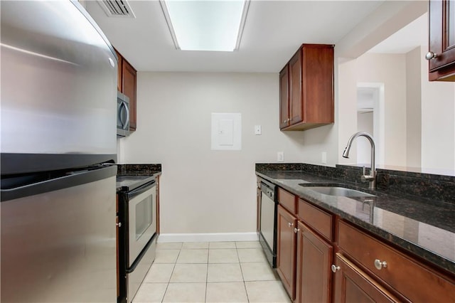 kitchen with appliances with stainless steel finishes, light tile patterned floors, sink, and dark stone countertops