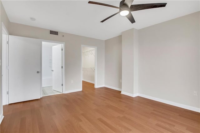 unfurnished bedroom with a closet, ensuite bath, a walk in closet, light hardwood / wood-style floors, and ceiling fan